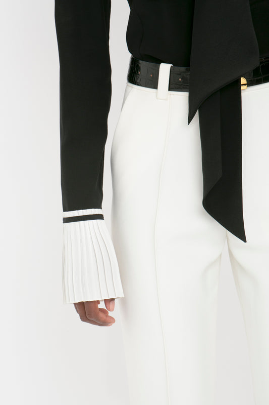 A person dressed in a stylish black blazer and Victoria Beckham cropped kick trousers in ivory with a focus on the pleated cuff detail and black belt.