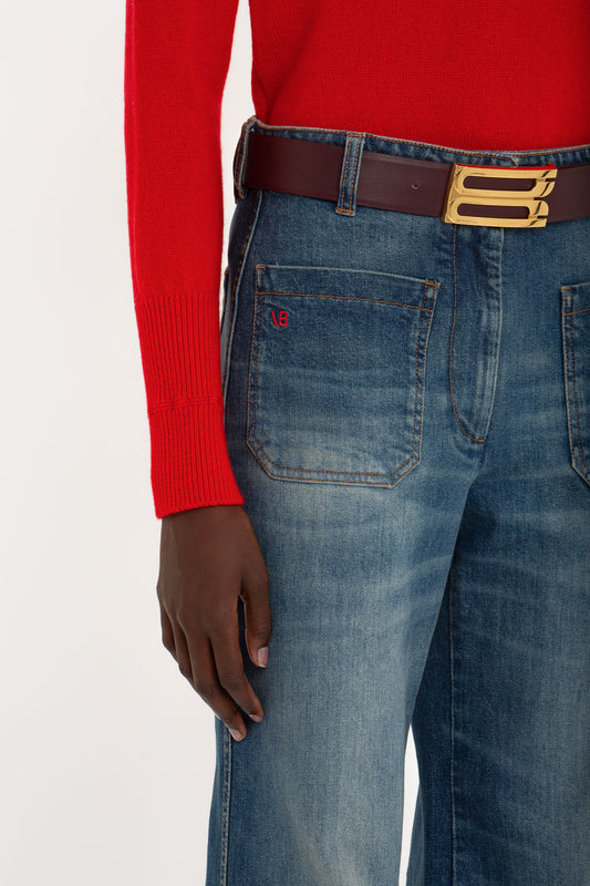 Close-up of a person wearing Victoria Beckham Alina Jean In Heavy Vintage Indigo Wash and a red sweater, focusing on the belt and back pocket with a visible "Vintage Indigo Wash" logo.