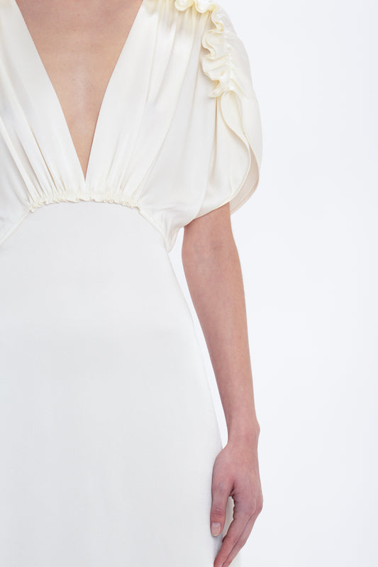 A person wearing a Victoria Beckham Exclusive V-Neck Ruffle Midi Dress In Ivory with puffy short sleeves stands against a plain white background. The dress features gathered fabric detailing at the shoulders and waist.