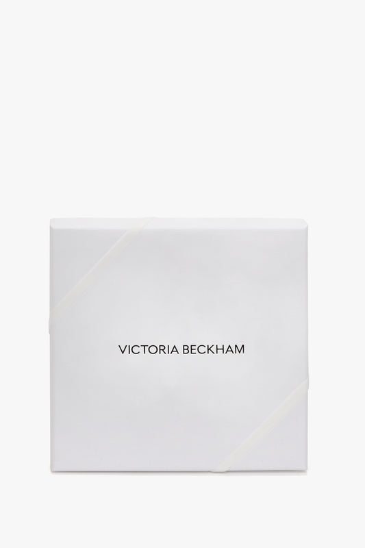 White gift box with a diagonal ribbon, labeled "Victoria Beckham Monogram Lace Tights In Black" in black text, on a plain white background.