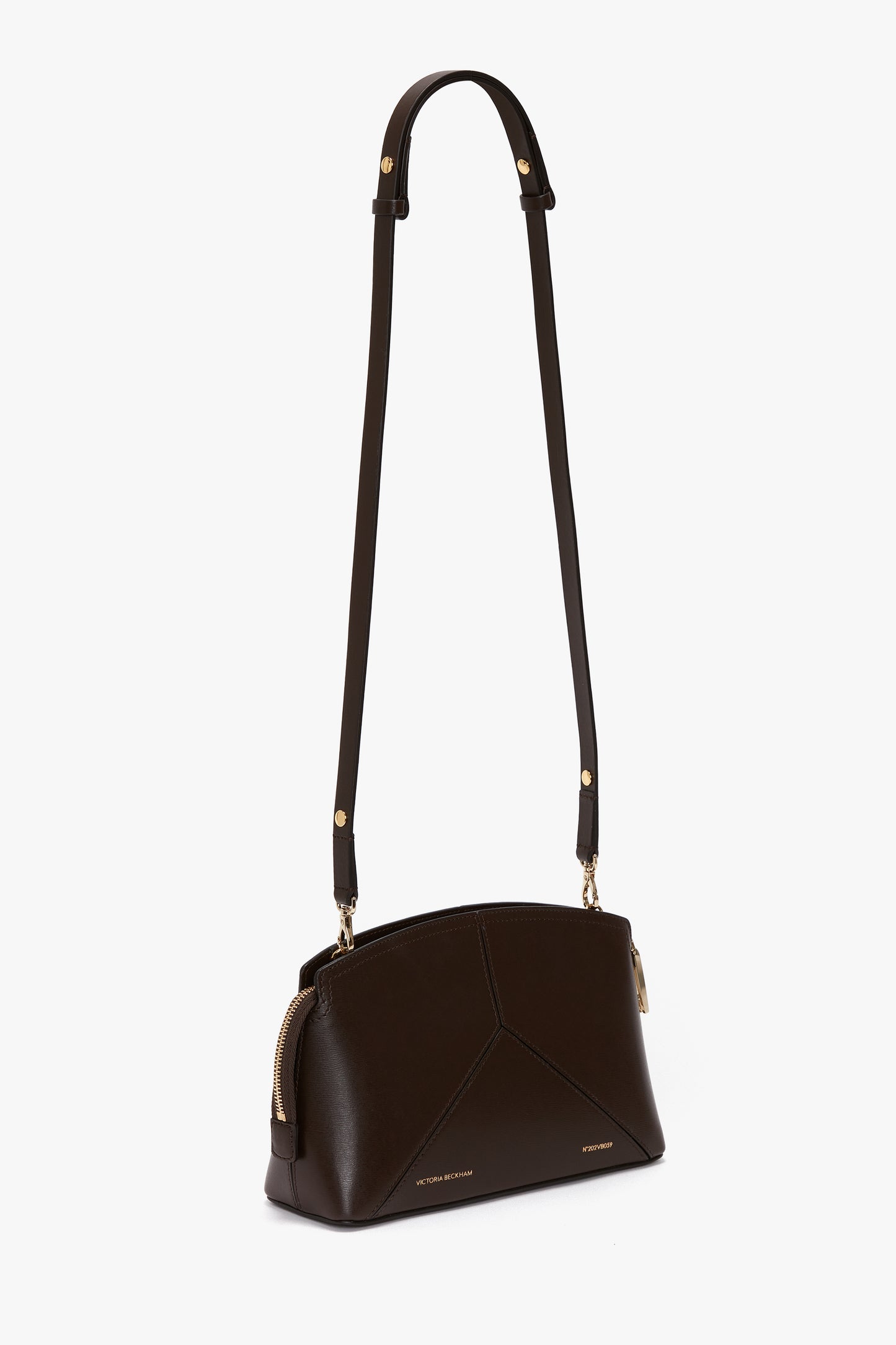Introducing the Exclusive Victoria Crossbody Bag In Brown Leather, a dark brown calf leather bag with gold accents and a long adjustable strap by Victoria Beckham. The bag features a zippered top closure and a structured, geometric design, perfect for any occasion.