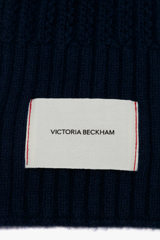 Close-up of a Victoria Beckham Exclusive Logo Patch Scarf In Navy on a dark blue knitted fabric.
