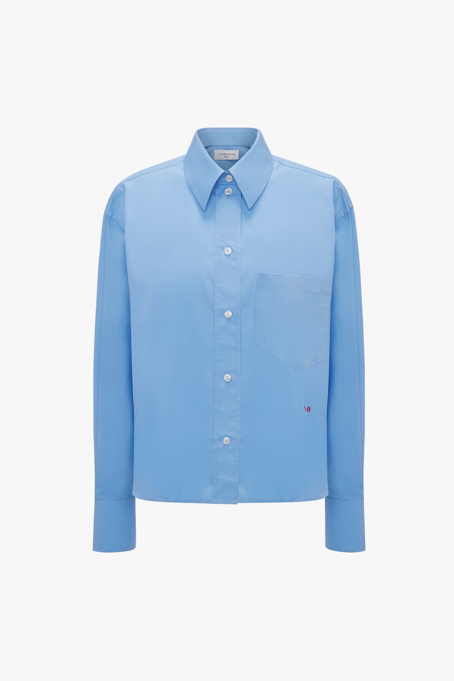 A Cropped Long Sleeve Shirt In Oxford Blue featuring a breast pocket and a small embroidered Victoria Beckham monogram near the pocket's bottom-right corner.