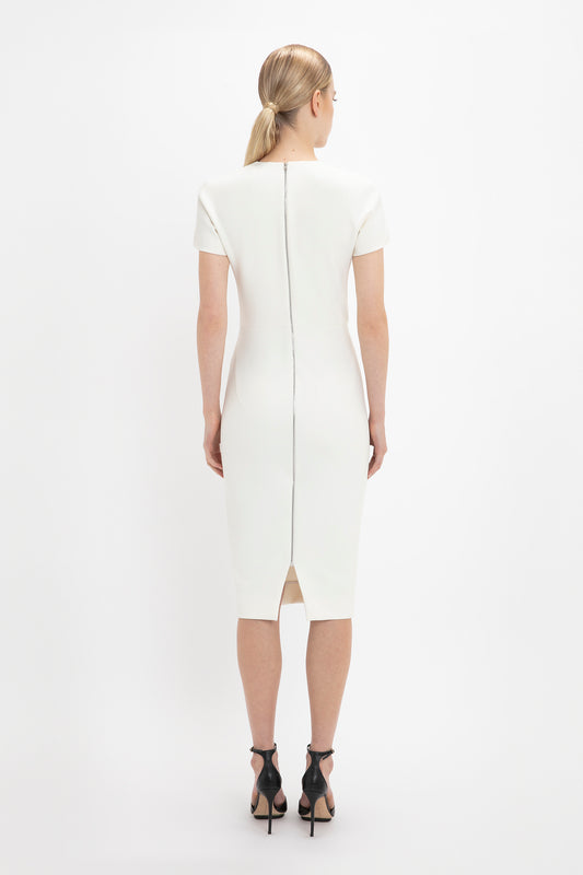 Woman in a Victoria Beckham fitted T-shirt dress in ivory viewed from the back, featuring a center back zipper and short sleeves, standing against a white background.
