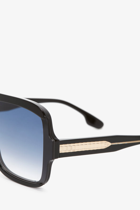 Close-up of a pair of Victoria Beckham Layered Mask Sunglasses In Black Gradient, featuring black lenses and black frames, with a detailed, textured temple on a white background.