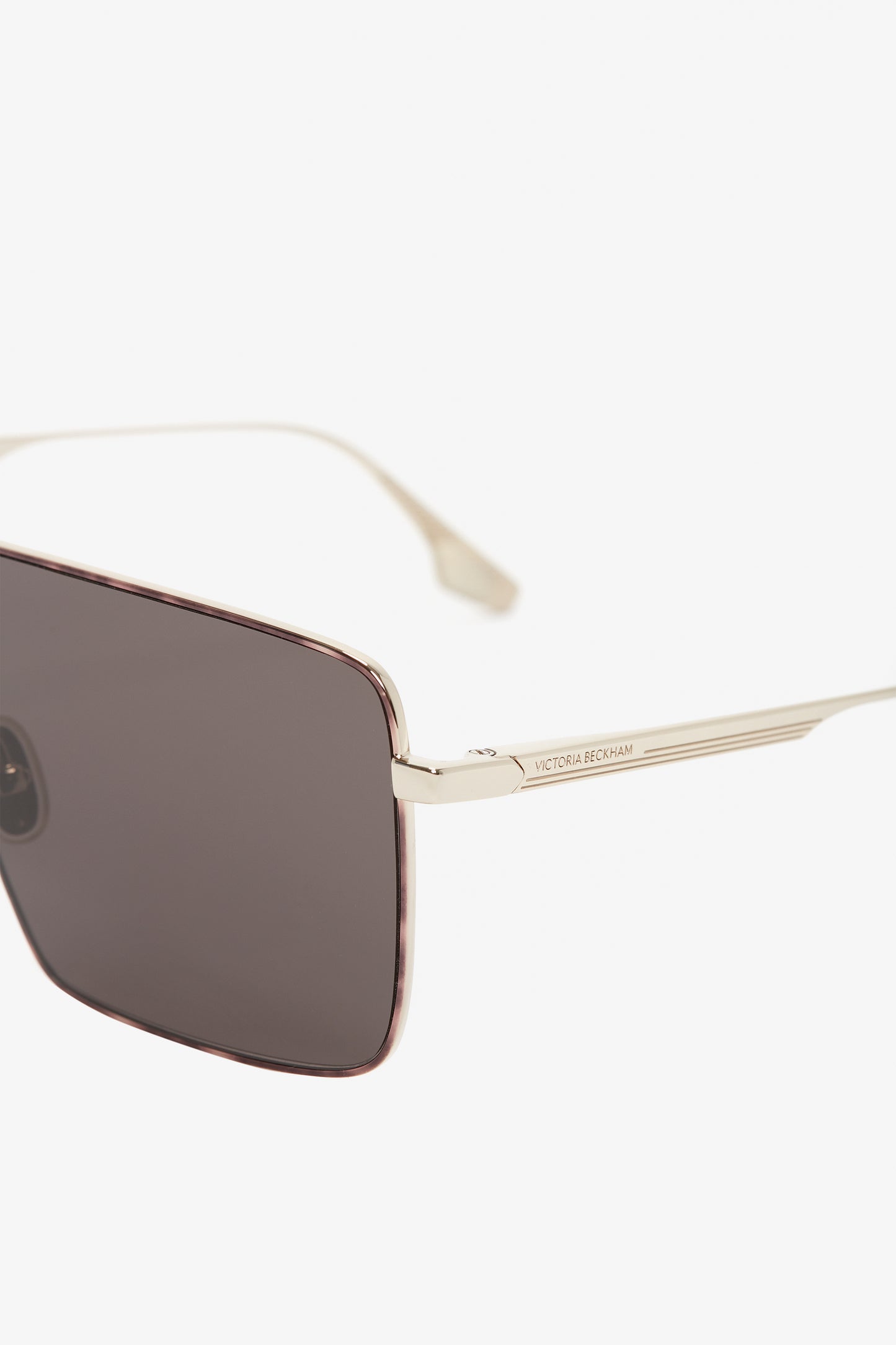 Close-up of a pair of Rectangular Visor In Gold-Smoke with dark lenses and gold-colored thin metal frames. The Victoria Beckham logo is inscribed on the arm.