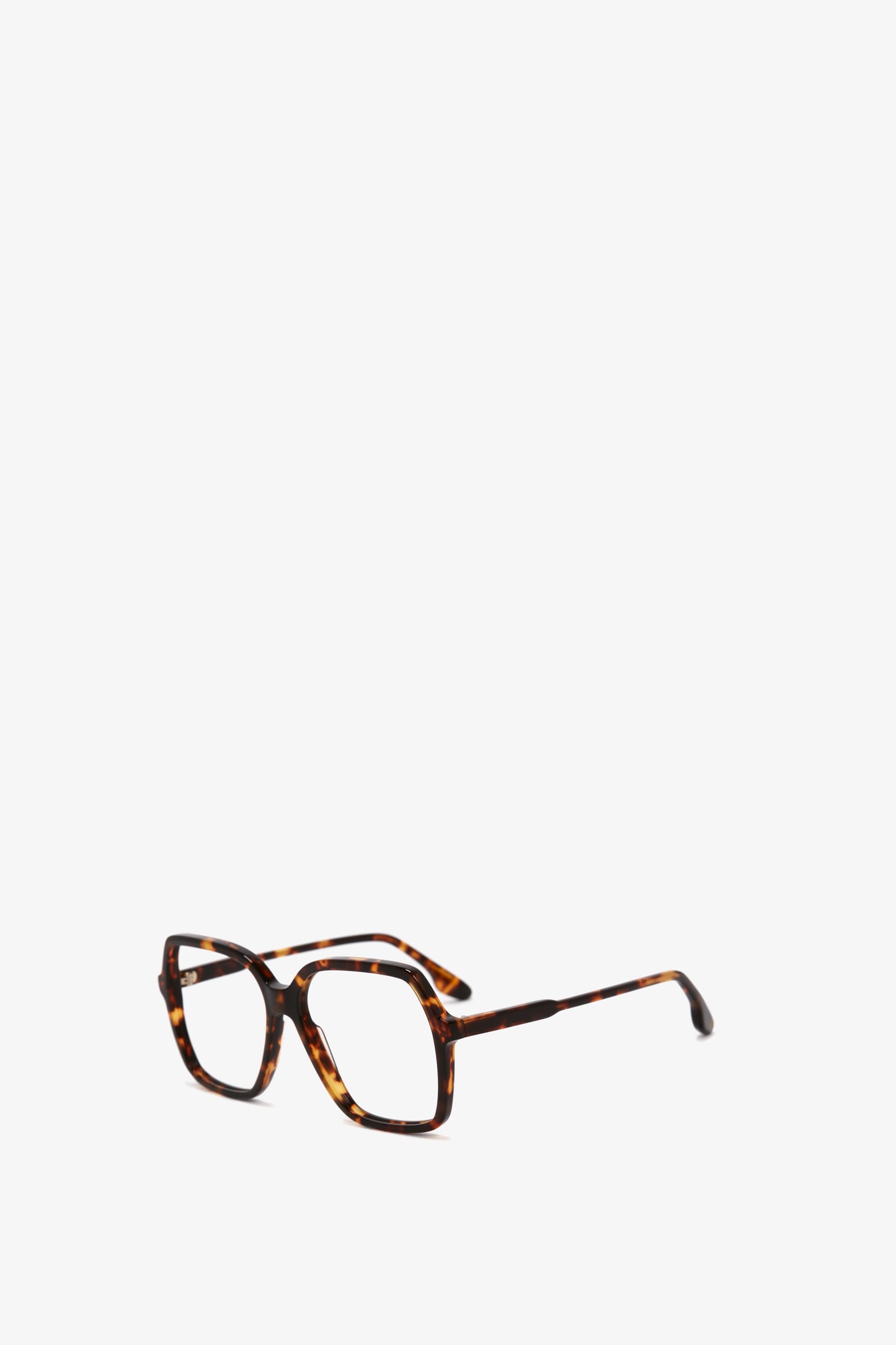 A pair of Guilloche Frame Opticals In Dark Havana in Dark Havana tortoise acetate with thin arms and clear lenses, set against a white background from the Victoria Beckham Eyewear collection.