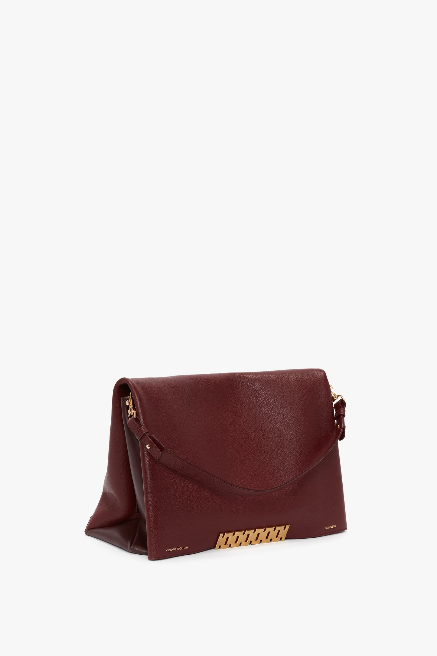 A Victoria Beckham Jumbo Chain Pouch Bag In Bordeaux Leather with a gold clasp and decorative details stands on a white surface, featuring grained leather and a detachable strap.