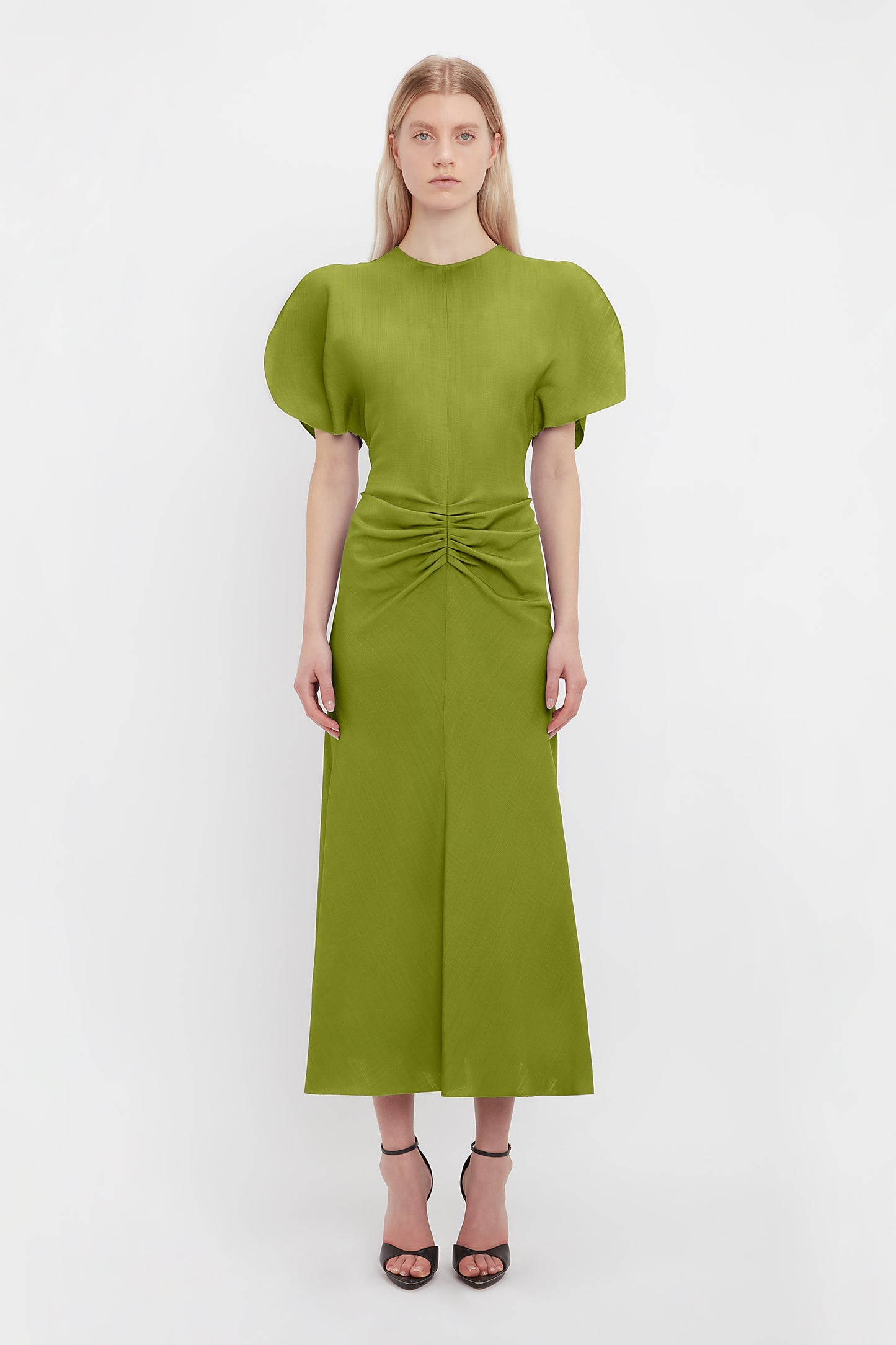 Model wears the green dress worn by Bella Hadid in the Victoria Beckham Paris Fashion Show. With a gathered front, midi length and soft flared skirt. A wedding dress guest piece from luxury designer VB. 